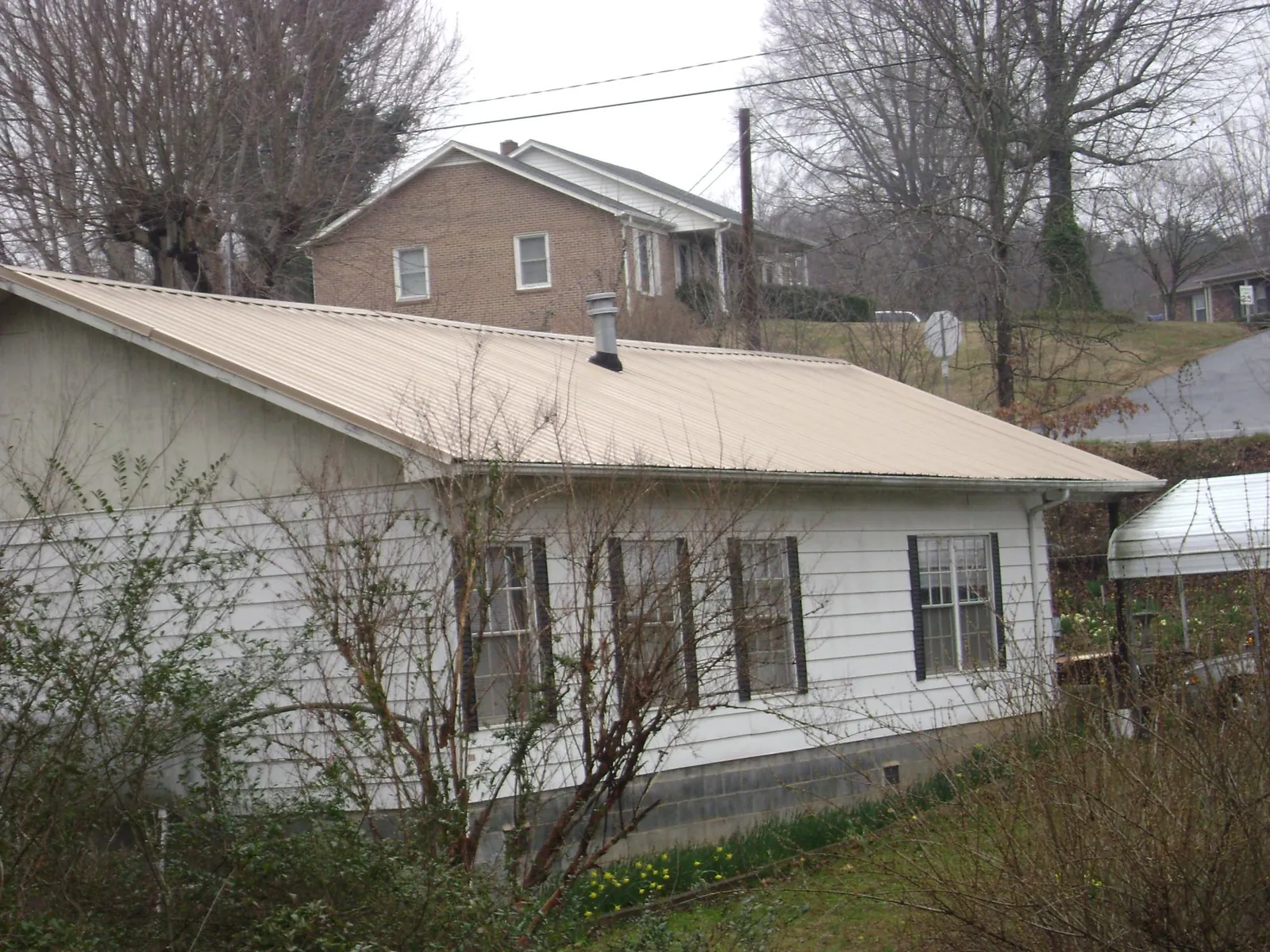 Tan metal roof on a white sided house set into a hillside — Commercial Roofing by Roofing Brothers in Wellington