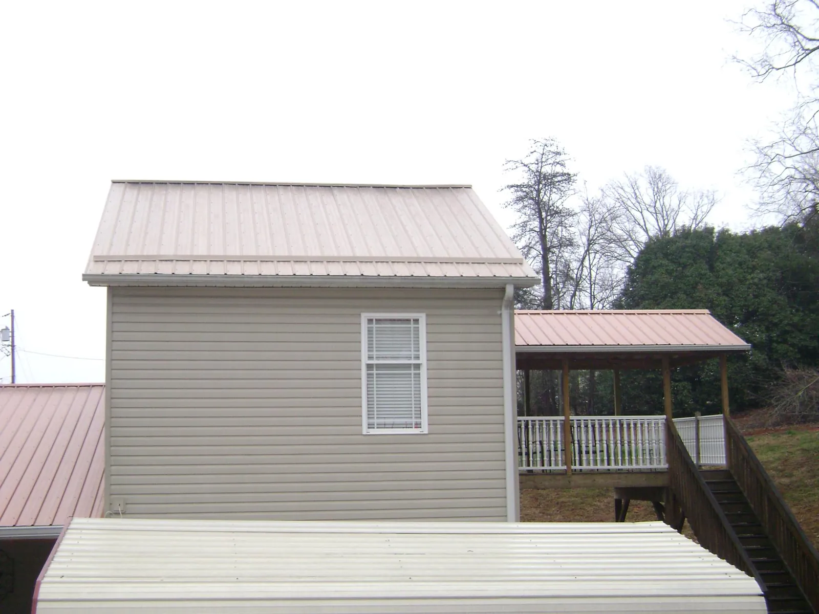Tan metal roofs on a two story addition and attached porch, from a Roof Replacement job in Wellington